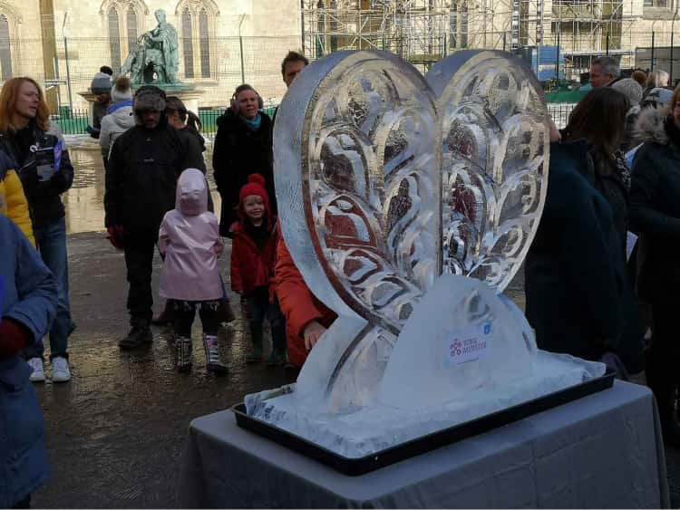 A photo of an ice sculpture heart outside of York Minster with crowds in the background looking at it.