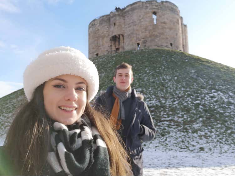 Myself and Naomi wrapped up in winter coats and scarves, stood in front of a snowy Clifford's tower