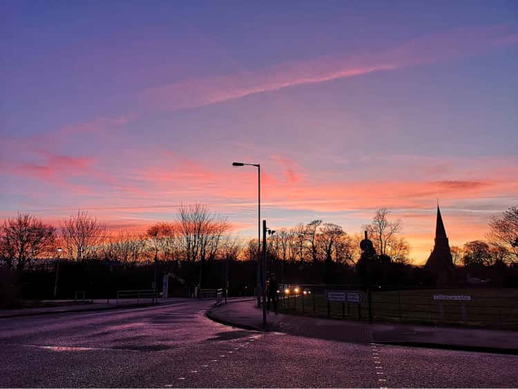 The silhoutte of the trees and Heslington Church are in the foreground, while the background is a deep blue sky and light pink clouds, just before sunset.