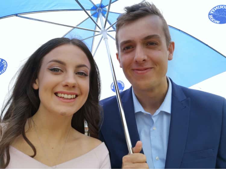 Myself (dressed in a blue suit) and Naomi (in a pink dress) for her graduation, with a large umbrella covering us as we try to stay dry in the rain.