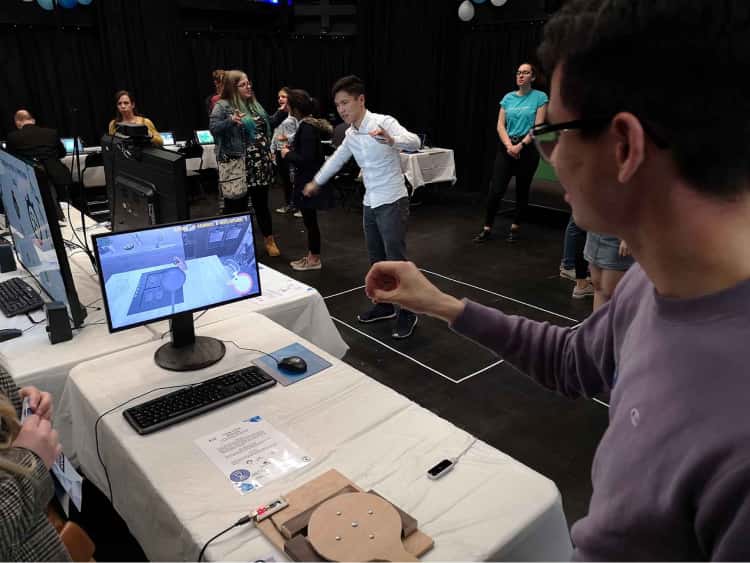 My friend James, stood in front of a student project at the Interactive Media Showcase. James has his arm raised as he tried to use the motion controls to cook a meal as instructed by the game he is playing on screen.