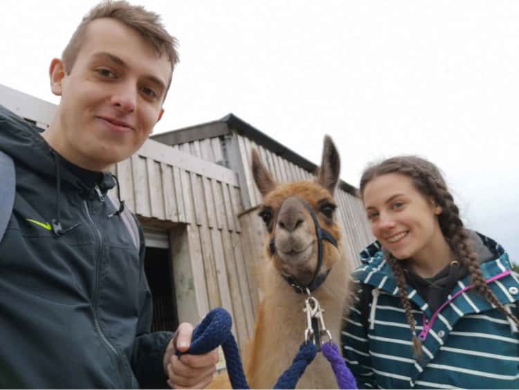 Myself and Naomi stood either side of a Llama (called Sid), that we walked. Somehow we're all smiling, stood in front of a wooden shed.