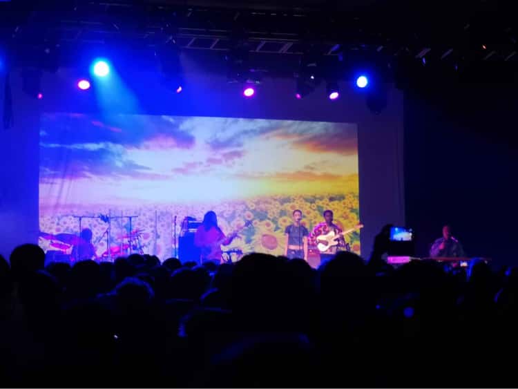 The band, The Internet, performing on stage in Manchester in front of a sunflower background.