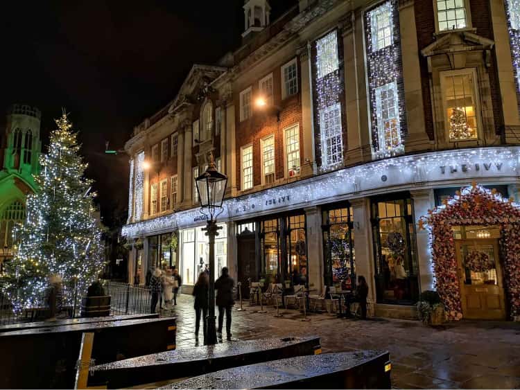 A photo of St Helen's Square, York at nighttime. A christmas tree is to the left of the picture, lit up in gold and white lights, with the restaurant, The Ivy, to the right, also covered in white lights.